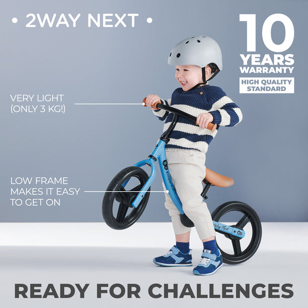 Smiling child riding blue Kinderkraft Balance Bike 2WAY NEXT with helmet.