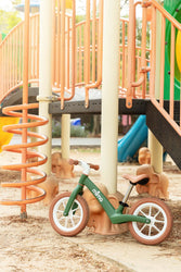 mima ZOOM Lite Balance Bike beside playground equipment, designed for kids' mobility and balance skills.