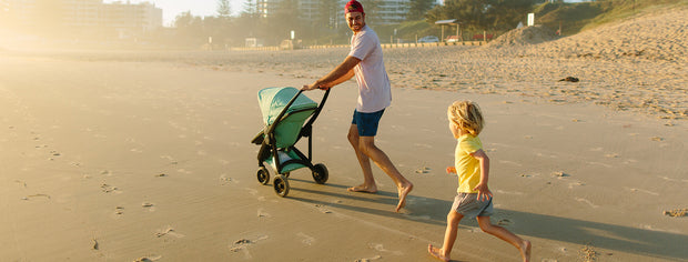 Man and child walking with teal Greentom Reversible Stroller on beach at sunset.