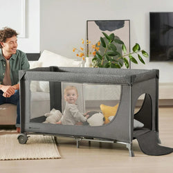 Baby playing in Kinderkraft Cot JOY 2, father smiling nearby in a modern living room.