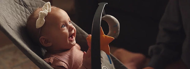 Baby smiling in a grey Kinderkraft baby bouncer MIMI