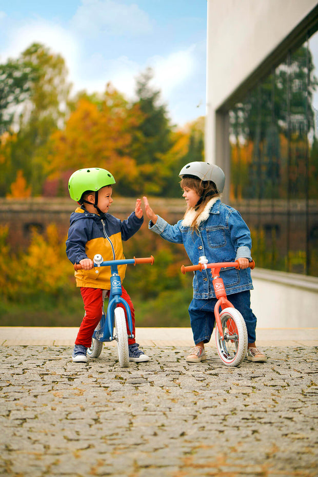 Two children high-fiving, each on the Kinderkraft Balance Bike Rapid.