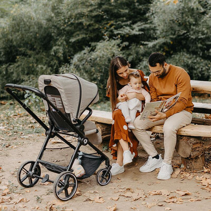 Parents sitting on a bench in park with the Coccolle Travel System LISSIA 