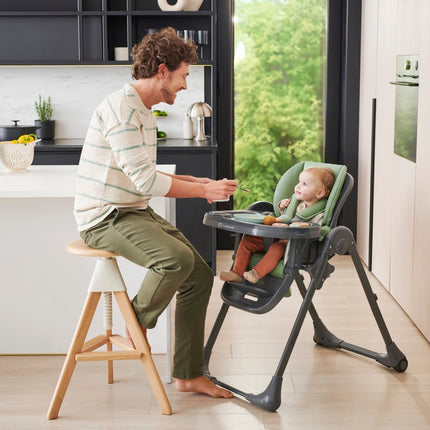 Parent feeding his baby sitting inside the Kinderkraft High Chair TUMMIE 2 in Green