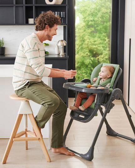 Parent feeding his baby sitting inside the Kinderkraft High Chair TUMMIE 2 in Green