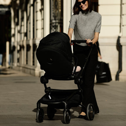 Parent using the Mima Creo Stroller Black in a stylish urban setting.