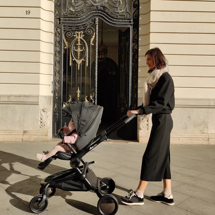 Woman in black with toddler in pink using Mima Creo Stroller Black during a walk outside a historic entrance.