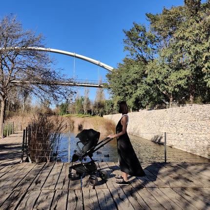 Woman in long black dress with Mima Creo Stroller Black and toddler by the lake on a sunny day.