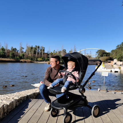 Man in brown with toddler using Mima Creo Stroller Black watching ducks by the water in the park.