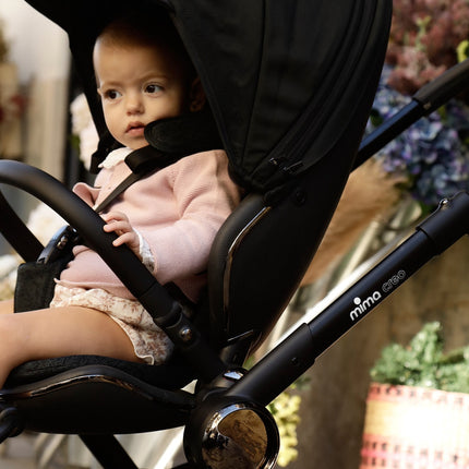 Child sitting comfortably in a Mima Creo Stroller Black in an urban setting.