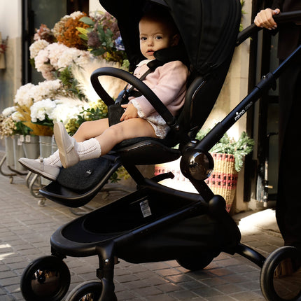 Parent pushing a Mima Creo Stroller Black with a child in an urban area.