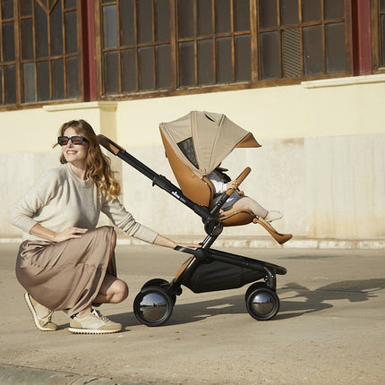 Woman pushing Mima Creo Stroller Mocha with child, outdoor stroll.