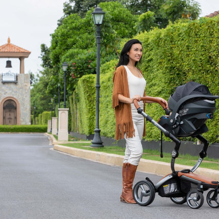 Smiling woman pushing Mima iZi GO Modular X1 Car Seat in garden.