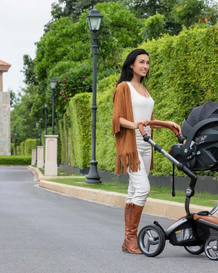 Smiling woman pushing Mima iZi GO Modular X1 Car Seat in garden.