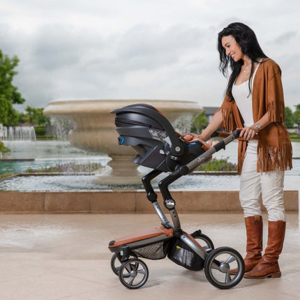 Smiling woman with Mima iZi GO Modular X1 Car Seat by fountain.