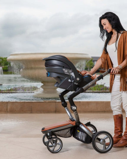 Smiling woman with Mima iZi GO Modular X1 Car Seat by fountain.