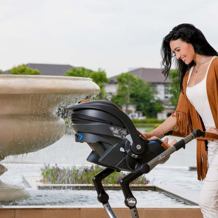 Smiling woman with Mima iZi GO Modular X1 Car Seat by fountain.