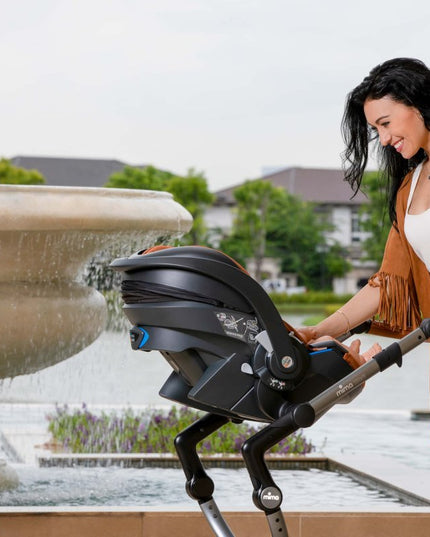 Smiling woman with Mima iZi GO Modular X1 Car Seat by fountain.