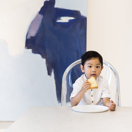 Boy eating sandwich in Mima Moon High Chair with abstract painting in background