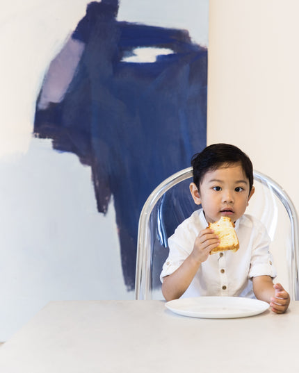 Boy eating sandwich in Mima Moon High Chair with abstract painting in background