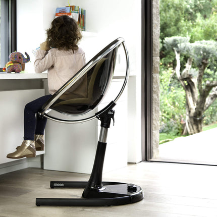 Side view of a child sitting in a Mima Moon High Chair, engaged with toys at a desk.