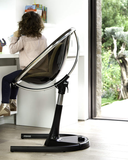 Side view of a child sitting in a Mima Moon High Chair, engaged with toys at a desk.