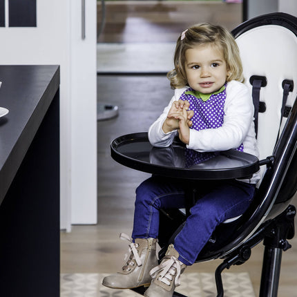 Child enjoying a snack in a Mima Moon High Chair with a white cup and cookies on the table.