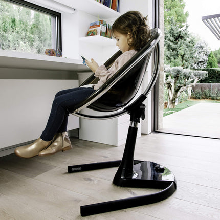 Child using a Mima Moon High Chair while looking at a phone by a window