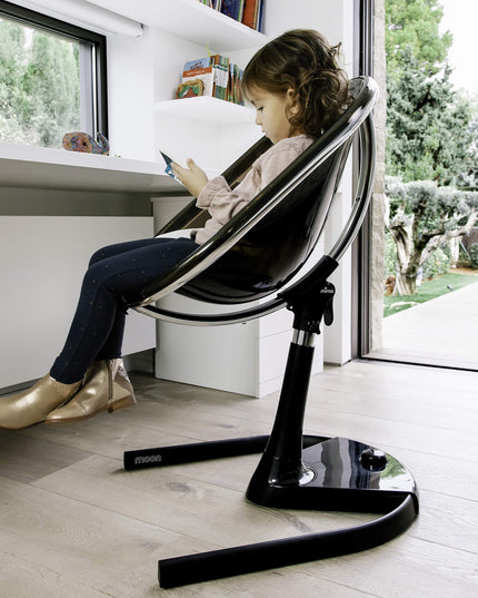 Child using a Mima Moon High Chair while looking at a phone by a window