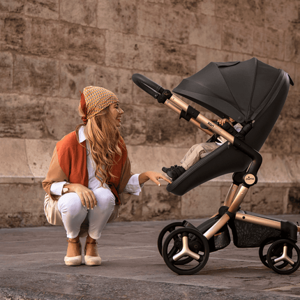 Mother pushing Mima XARI MAX stroller in front of historic stone facade.