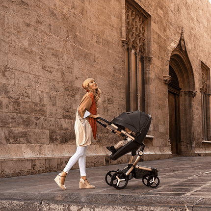 Stylish woman with Mima XARI MAX stroller in front of historic stone architecture.