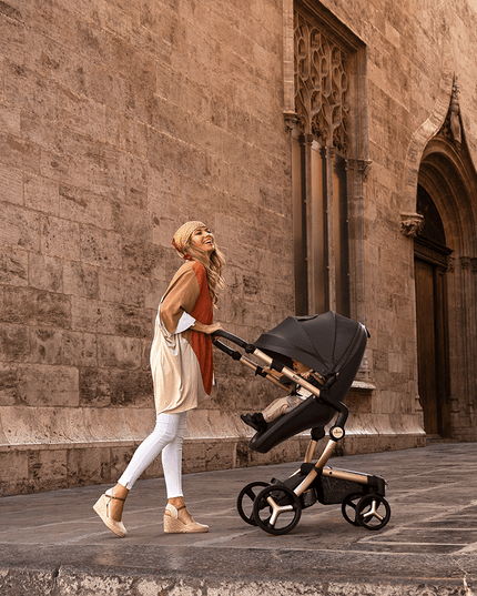 Stylish woman with Mima XARI MAX stroller in front of historic stone architecture.