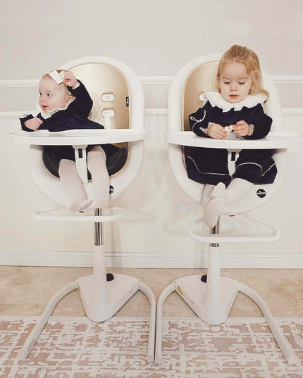 Two toddlers in matching outfits sitting in Mima Moon High Chairs.