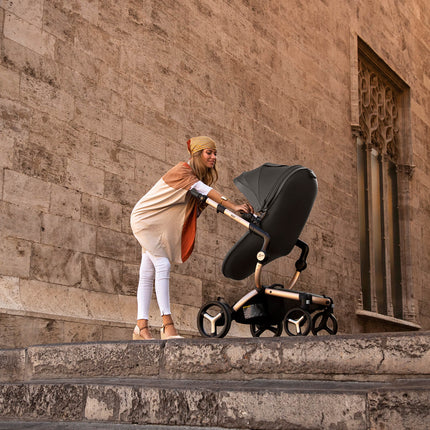 Woman with headscarf interacting with child in Mima XARI MAX stroller by historic building.