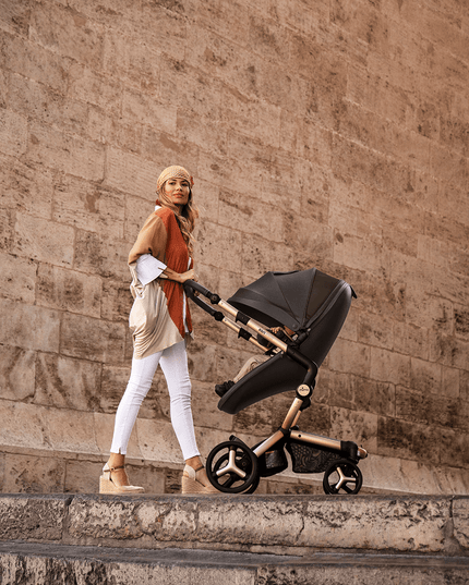 Woman in headscarf pushing Mima XARI MAX stroller in historic urban setting.