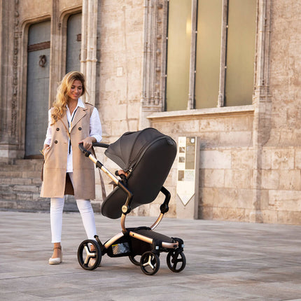 Woman with Mima XARI MAX stroller in front of historic stone building.