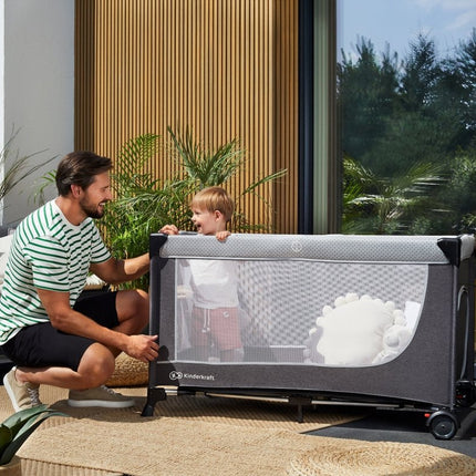 Father and child interacting beside Kinderkraft Travel Cot LEODY outdoors